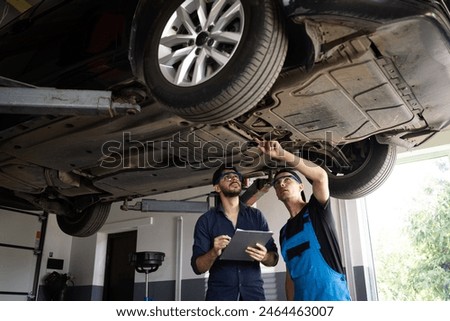 Manager Checks Data on a Notebook and Explains the Breakdown to a Mechanic. Car Service Employees Inspect the Bottom and Skid Plates of the Car. Modern Workshop. Auto Service.