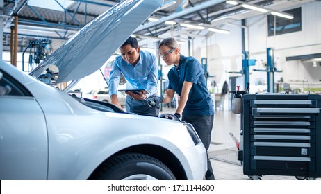 Manager Checks Diagnostics Results on a Tablet Computer and Explains an Engine Breakdown to an Female Mechanic. Car Service Employees Inspect Car's Engine Bay with a LED Lamp. Modern Clean Workshop. - Powered by Shutterstock