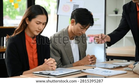 A manager confronts two dejected Asian professionals at a conference table, illustrating workplace conflict, failed planning, and team accountability in a corporate setting.