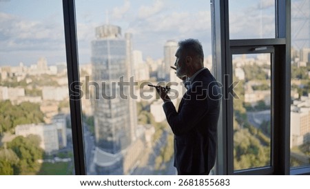 Manager creating voice message on mobile phone standing by panoramic window business center. Senior businessman talking in cellphone loudspeaker. Elegant employee dictating audio notes in smartphone.