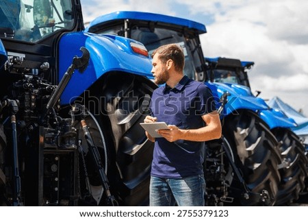 Manager with digital tablet inspecting new tractors at a machinery dealership.