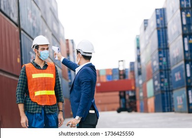 Manager or engineer foreman using infrared thermometer measure temperature to construction site staff worker at shipping container warehouse. men at work wearing face mask prevent Covid-19 infection