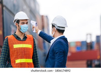 Manager or engineer foreman using infrared thermometer measure temperature to construction site staff worker at shipping container warehouse. men at work wearing face mask prevent Covid-19 infection