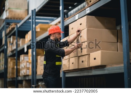 Manager or engineer man employee using tape measure for measuring dimension of product in cardboard box. Worker wearing high visibility clothing, helmet checking goods or boxes for delivery.