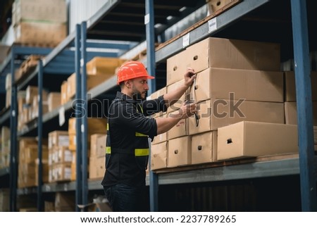 Manager or engineer man employee using tape measure for measuring dimension of product in cardboard box. Worker wearing high visibility clothing, helmet checking goods or boxes for delivery.