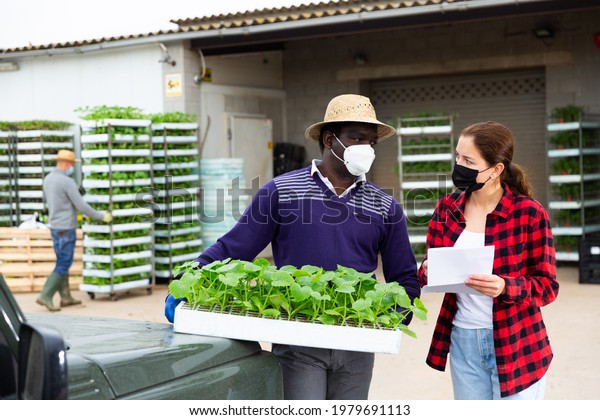 Manager and farmer in protective\
mask signing papers and communicating near car. High quality\
photo
