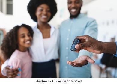 Manager Giving New Car Key To Young Black Family At Auto Dealership Store, Selective Focus. Happy African American Customers Buying Vehicle From Salesman At Automobile Showroom