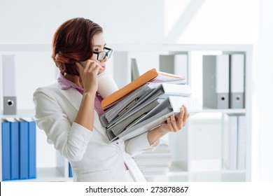 Manager holding stack of folders, and coffee while talking on the phone