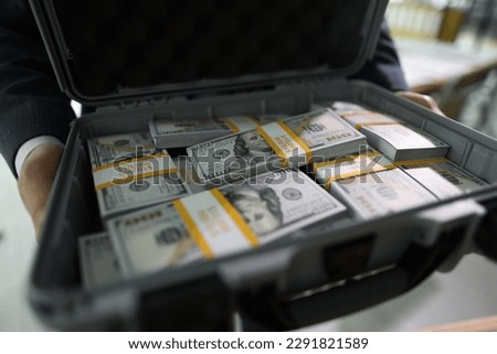 Manager holds open case with counted stacks of dollar banknotes in hands. Man shows briefcase with money paid for successful deal by client