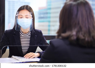 Manager From HR Department Wearing Facial Mask Is Interviewing New Applicant And Reading Her Resume And Profile Through The Partition For Social Distancing And New Normal Policy