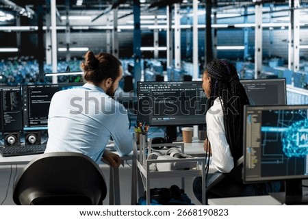 Manager and intern in server room using PC to review infrastructure diagnostics. IT specialist and trainee in data center analyzing performance data to maintain system uptime