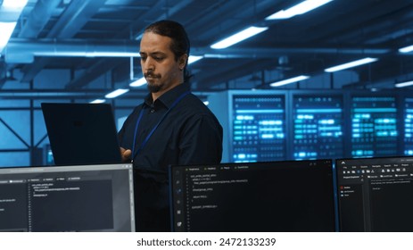 Manager overseeing server room, running code on laptop, troubleshooting and upgrading technologically advanced hardware clusters. System administrator programming in server farm - Powered by Shutterstock