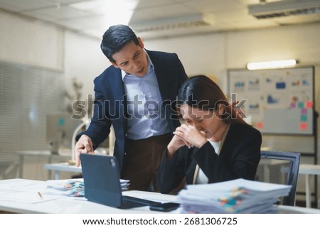 Manager pointing at a computer while scolding a crying businesswoman sitting at her office desk, highlighting workplace stress and conflict