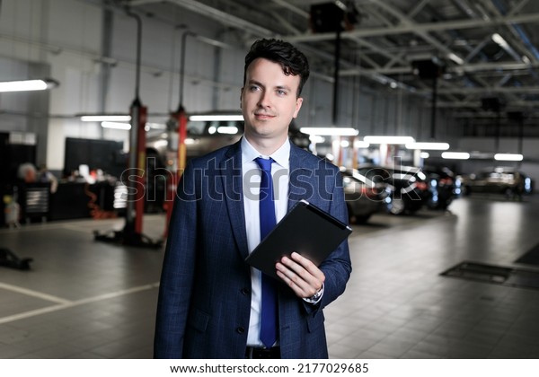 The\
manager for the reception of cars for repair with a tablet against\
the background of the service area of the\
dealership