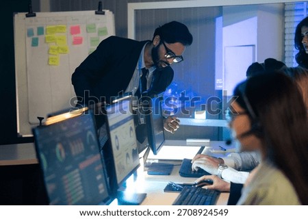 Manager, reviews data and reports on a computer screen, overseeing a diverse team in a high-pressure at command center or control room. executive is providing critical guidance on an urgent late night