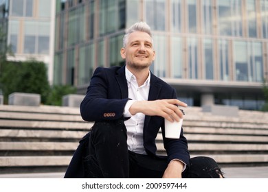 The Manager Is Sitting Near The Business Center Drinking A Coffee Break During Work. A Man Of European Appearance Is A Gray-haired Man. A Stylish Business Suit And A Good Irony.