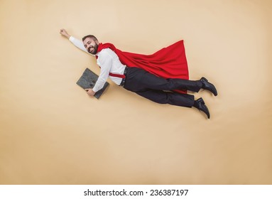 Manager In A Superman Pose Wearing A Red Cloak. Studio Shot On A Beige Background.