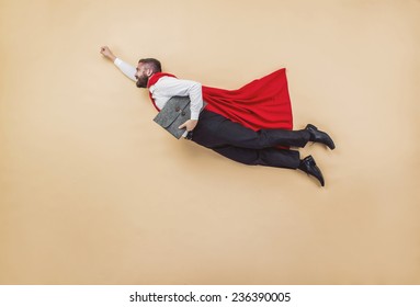 Manager In A Superman Pose Wearing A Red Cloak. Studio Shot On A Beige Background.