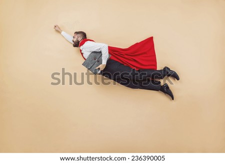 Manager in a superman pose wearing a red cloak. Studio shot on a beige background.