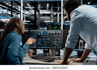 Manager supervises a technician coding in a server farm, overseeing repairs on data center racks used for computational operations.