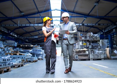 Manager Supervisor And Industrial Worker In Uniform Walking In Large Metal Factory Hall And Talking About Increasing Production.