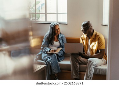 Manager and teammate collaborating on a project while sitting and discussing ideas with a laptop in a modern office environment. - Powered by Shutterstock