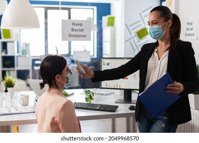 Manager using medical thermometer checking collegue temperature to prevent infection with coronavirus during global pandemic in startup business office. Teamwork with face mask against covid19