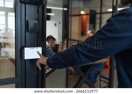 Manager using smart home system on mobile phone touchscreen, controlling lights and temperature in modern office