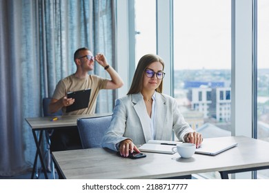 Manager Woman In Glasses Doing Office Work And Smiling, Successful Female Boss In Optical Glasses For Vision Correction, Posing At The Table. In The Background A Man