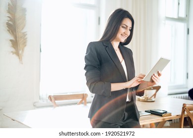 The manager works on a tablet computer. Business stylish black suit. Makes an order in the online store lunch food. In a modern office. The economist is a brunette woman.