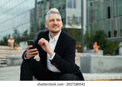 The manager writes a response to the client by email. A businessman is a gray-haired man in a business suit sitting near the new office. A lawyer communicates by phone with colleagues via SMS. - Powered by Shutterstock