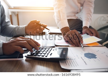 Managers using calculator to analyze sales cost reports and explain summary reports to employees calculate and record summary information data in the office.