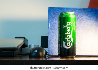 Manama / Bahrain - February 2, 2019: Carlsberg premium beer tin can placed on top of crowded messed office computer table with HP laptop and Bose speaker along with random miscellaneous.-Image