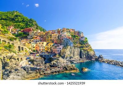 Manarola traditional typical Italian village in National park Cinque Terre with colorful multicolored buildings houses on rock cliff and marine harbor, blue sky background, La Spezia, Liguria, Italy