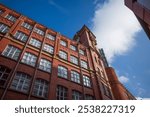 Manchester city center. Historic red brick building under a clear blue sky and fluffy clouds.