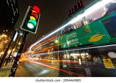 Manchester, England, UK. December 18th, 2021: An Electric Bus, Claiming To Put Out Zero Emissions Waits At The Lights. Long Exposure Showing Light Trails From Traffic. City Traffic, Rush Hour, Commute