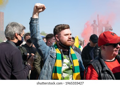 Manchester, UK. April 24, 2021. Protest Against Glazer And Super League At Old Trafford Football Ground. Fan Wearing Gold And Green Scarf With Fist In The Air. Trinity Statue In Background, Red Smoke.