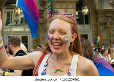 Manchester UK, August 28, 2019. Pride Parade Passing In Front Of Radisson Blue Hotel. Smiling Woman Wearing A Rainbow Necklace And Badge And Flag For Bisexual And Pansexual Community 