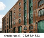 Manchester UK. Historic brick warehouse building with green doors and windows under a partly cloudy sky.