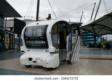 Manchester UK, July 24, 2022. Aurrigo Self Driving Auto-pod Trial At Etihad Campus. Driverless White Car In Rain With Text Centre For Connected And Autonomous Vehicles. 