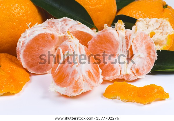 Mandarin orange, peeled from peel and divided\
into segments against the other tangerines, peel and leaves on a\
white surface\
