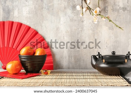 Mandarins with teapot, Japanese envelopes and fan on table against grey grunge background. New Year celebration