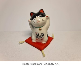 Maneki neko. The maneki-neko (招き猫, lit. 'beckoning cat') is a Japanese figurine which is often believed to bring good luck to the owner.Colors are white, black, red, and golden. Japanese cat figurine