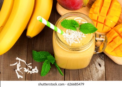 Mango, Banana, Coconut Smoothie In A Mason Jar Glass, Overhead View On A Rustic Wood Background