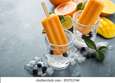 Mango banana popsicles on ice with fresh fruits and berries
