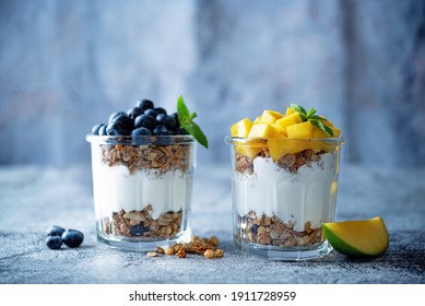 Mango  and blueberry Greek yogurt granola parfait in a glass. toning. selective focus