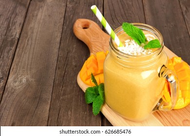 Mango coconut smoothie in a mason jar glass on paddle board against a rustic wood background
