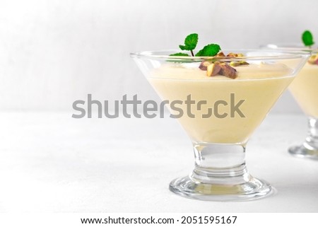 Mango dessert with yogurt topped with pistachio and mint in glass bowl on the white table. Copy space