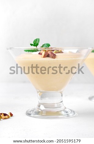 Mango dessert with yogurt topped with pistachio and mint in glass bowl on the white table