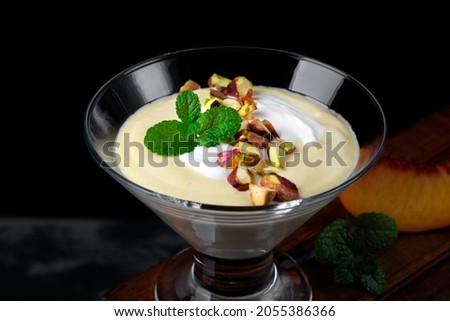 Mango dessert with yogurt topped with pistachio and mint in glass bowl against the black background. Exquisite dessert